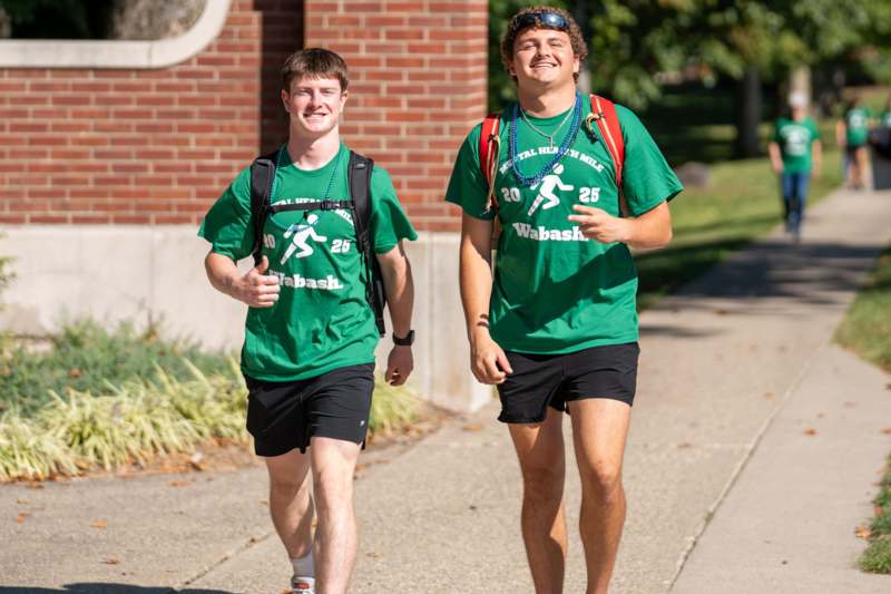two men wearing green shirts and backpacks walking down a sidewalk