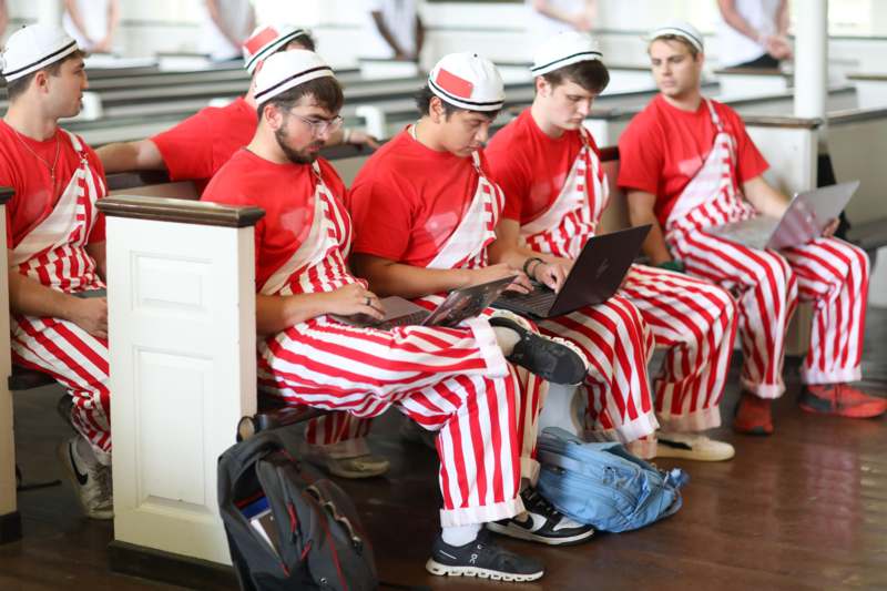a group of men in striped red and white outfits sitting on pews
