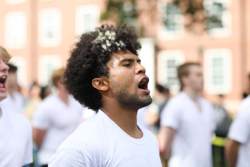 a man with a white shirt and black hair with white flowers on his head