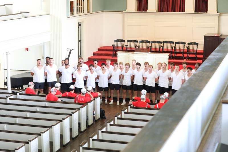 a group of people in white shirts and shorts singing in a church