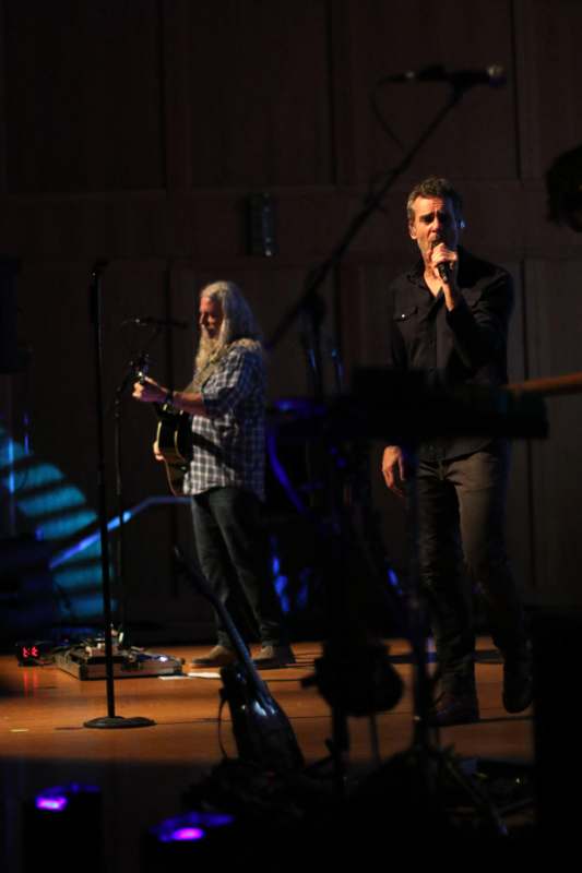 a man singing into a microphone with a man playing guitar