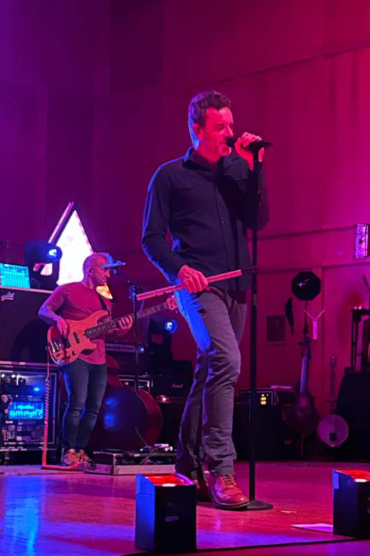 a man singing into a microphone with a guitar and other instruments