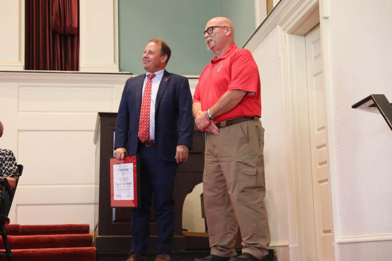 a man in a suit holding a certificate and standing next to another man