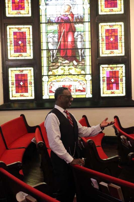 a man in a vest and tie in front of a stained glass window