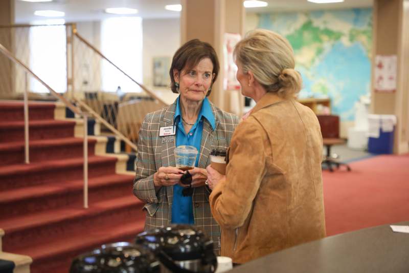 a woman holding a cup of coffee and another woman standing in a room