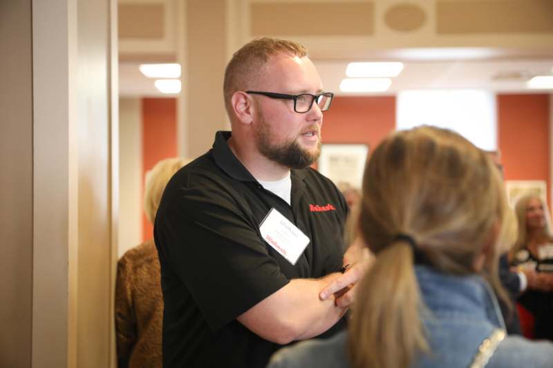 a man wearing glasses and a badge standing in a room with other people