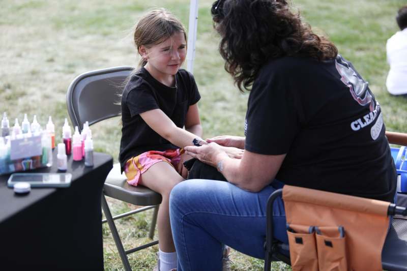a woman sitting in a chair with a girl painted her hand