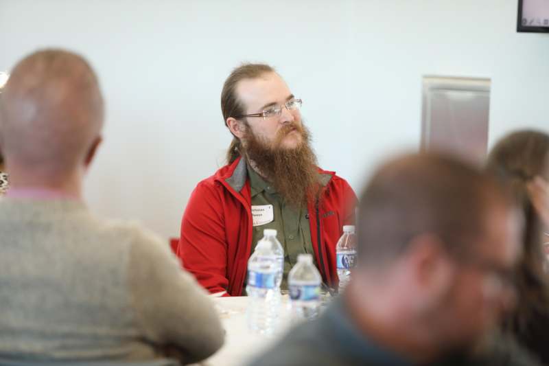 a man with a beard sitting at a table with water bottles and a computer