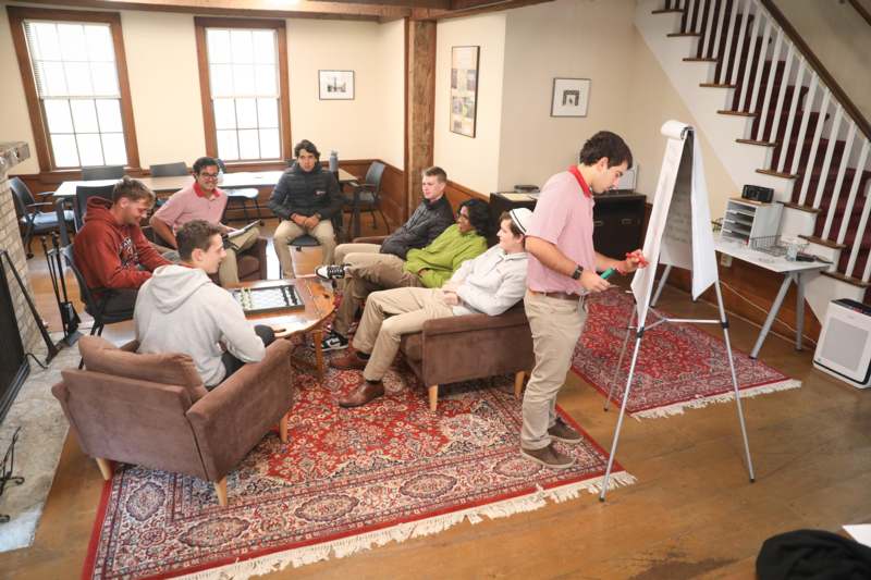 a group of people sitting in chairs and a man standing in front of a whiteboard