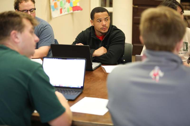 a group of people sitting around a table with laptops