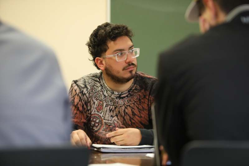 a man wearing glasses sitting at a table with other people in the background