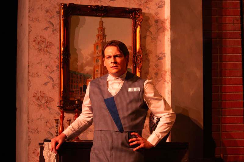 a man in a vest standing in front of a painting