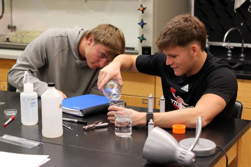 a couple of men pouring liquid into a glass
