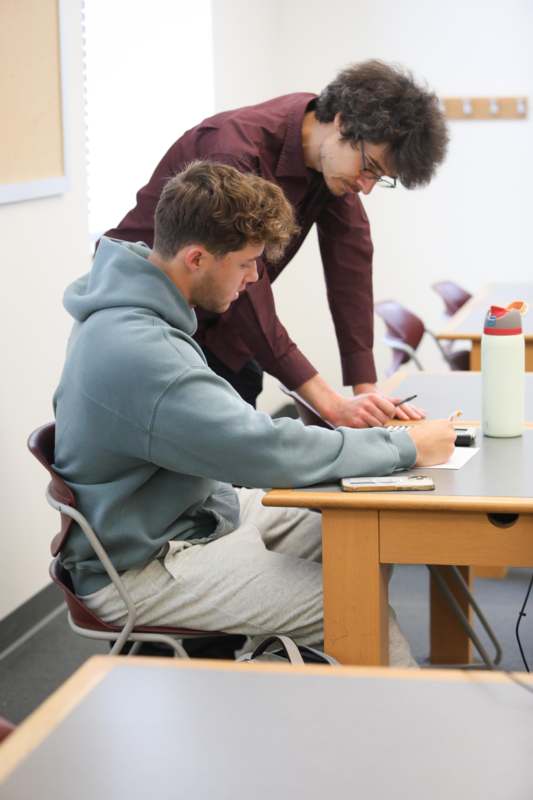 a man looking at a man writing on a paper