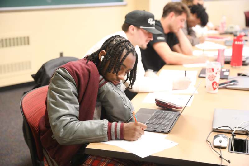 a man writing on paper in front of a laptop