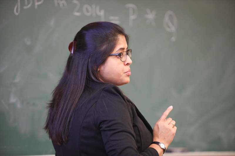 a woman in a black suit pointing at a chalkboard