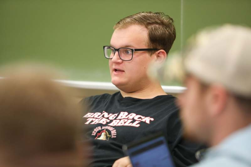 a man in glasses sitting in front of a green board
