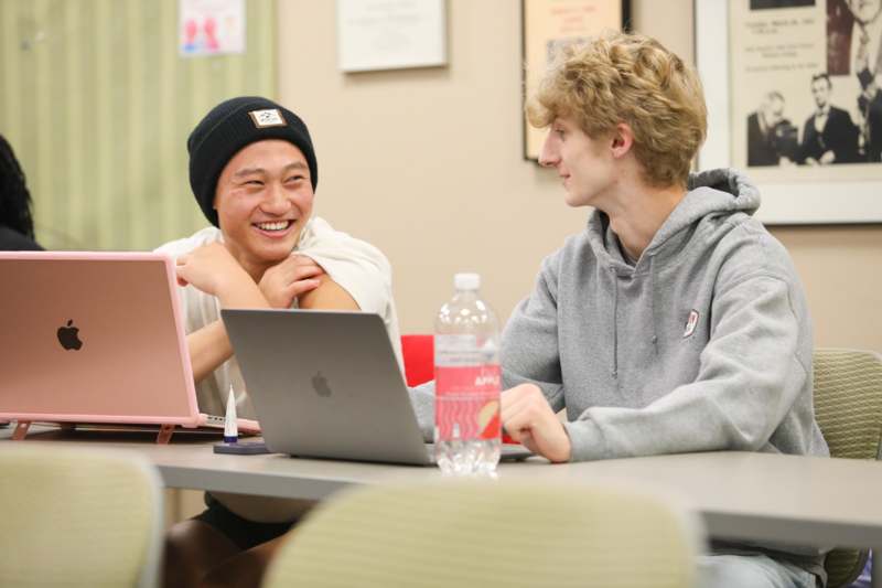 two men sitting at a table with laptops