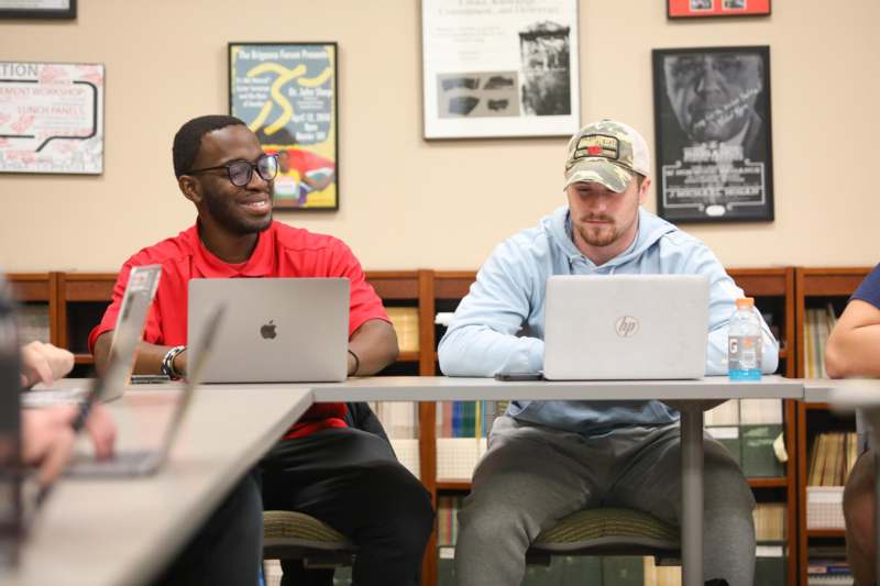 two men sitting at tables with laptops