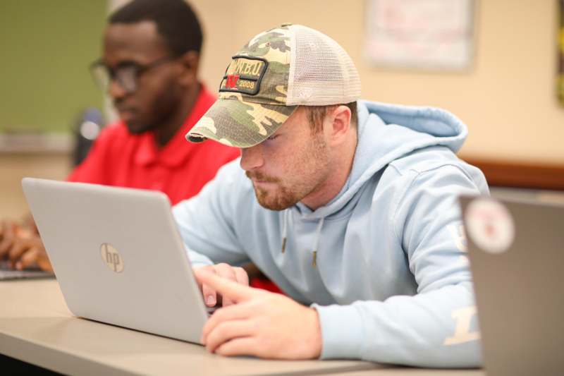 a man in a blue sweatshirt and a baseball cap using a laptop