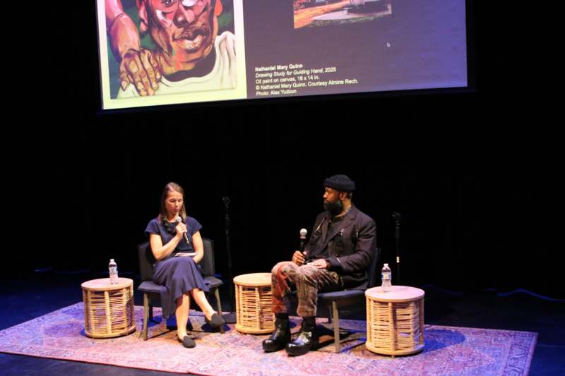 a man and woman sitting on a stage with a projector screen