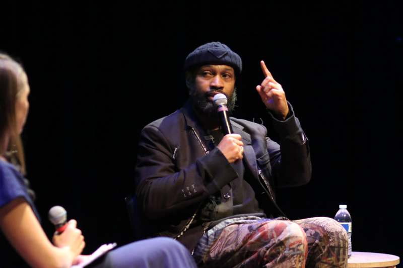 a man sitting on a stage holding a microphone