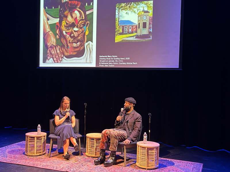 a man and woman sitting on a stage with a projector screen