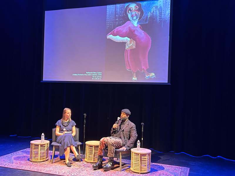 a man and woman sitting on a stage with a large screen
