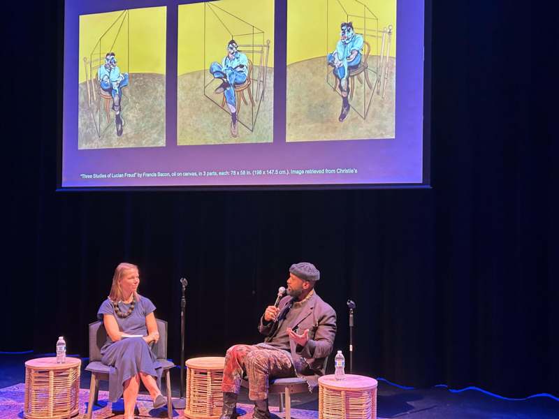 a man sitting in front of a screen with a woman in the background