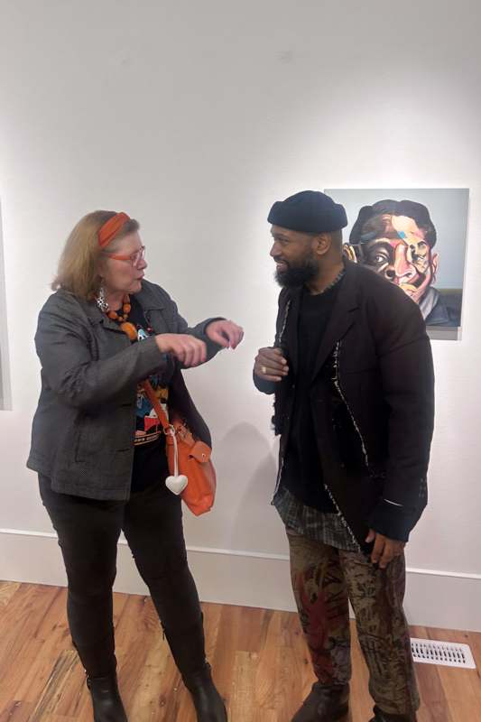 a man and woman standing in a room with paintings on the wall