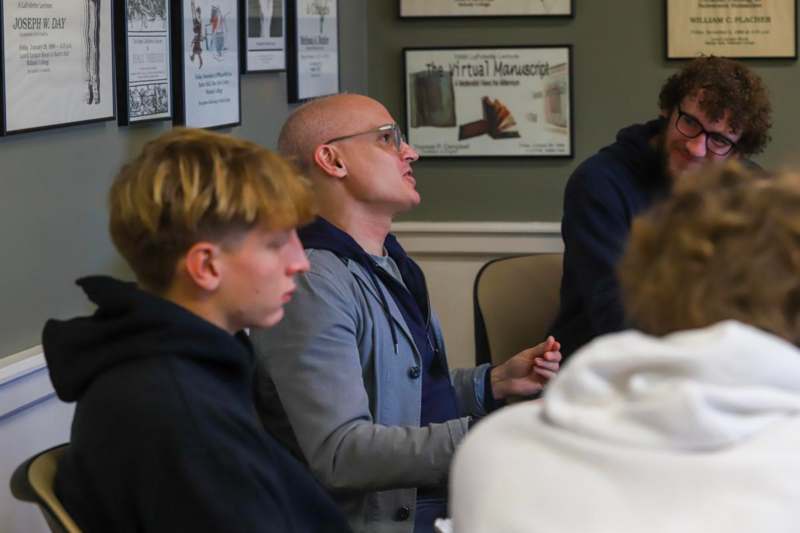 a man in a grey jacket sitting in a room with a group of people