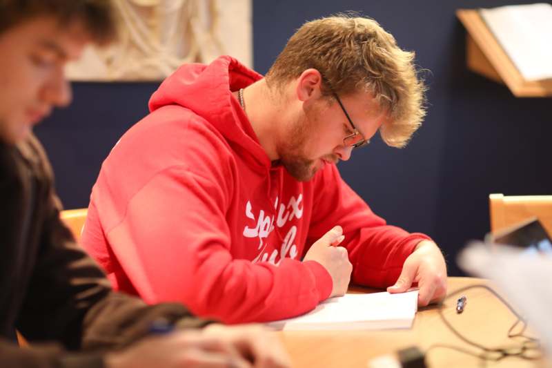 a man in a red sweatshirt writing on a paper