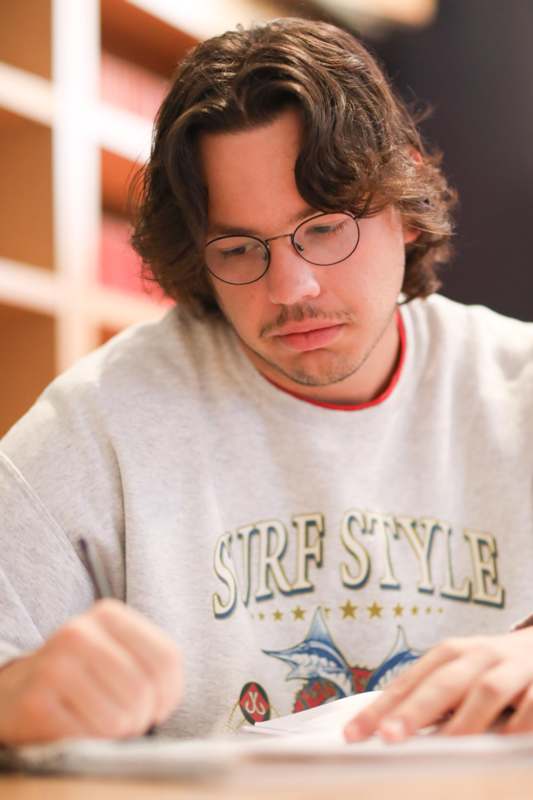 a man wearing glasses and writing on a paper