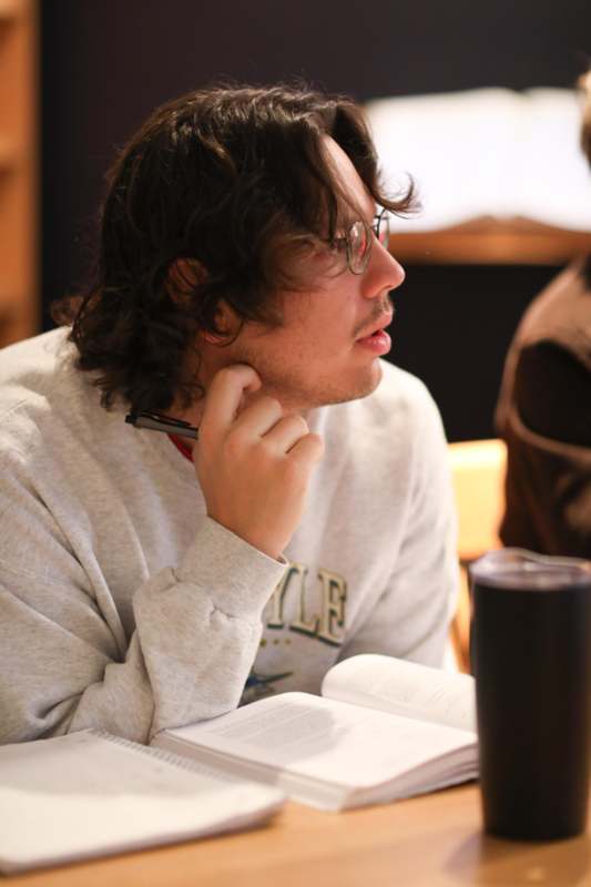 a man with glasses holding a pen and looking away