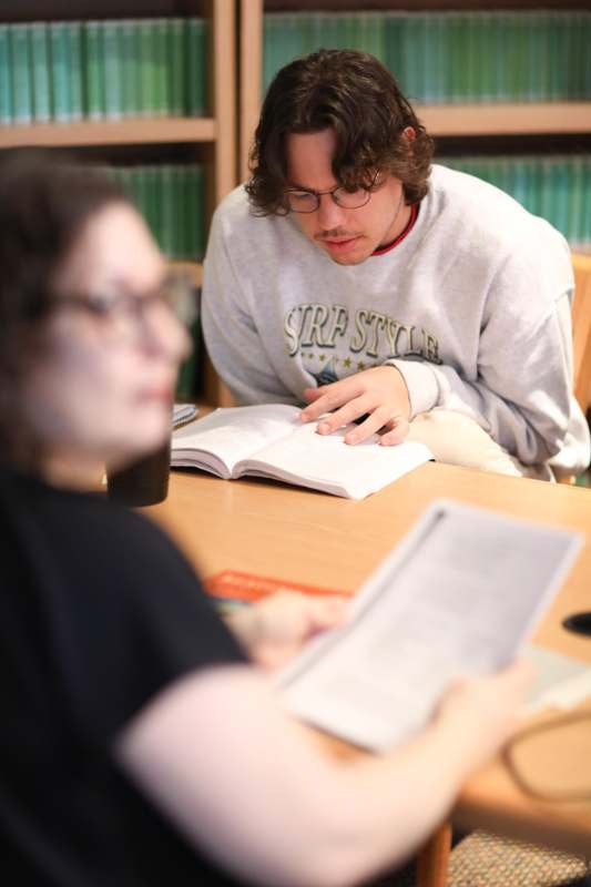a man and woman sitting at a table reading a book
