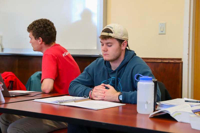 a man sitting at a table with papers and a whiteboard