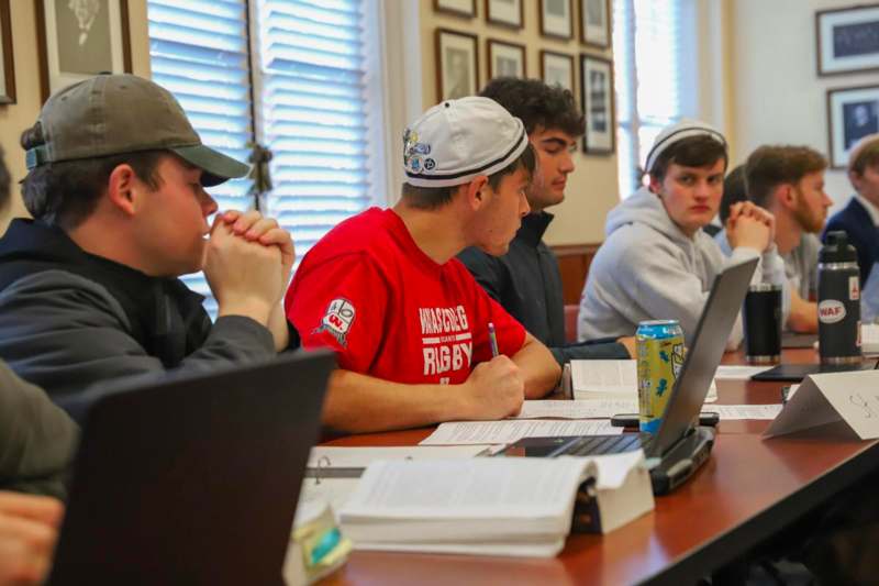 a group of people sitting at a table with laptops and books
