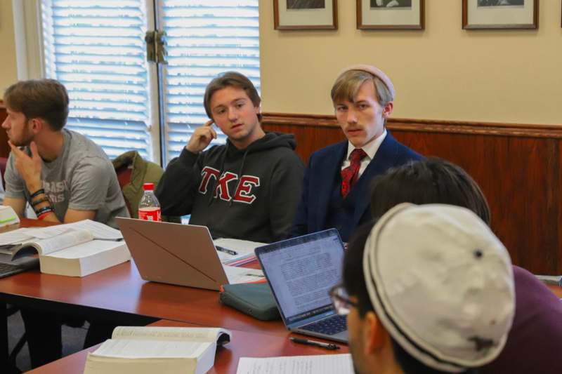 a group of people sitting around a table with laptops and books