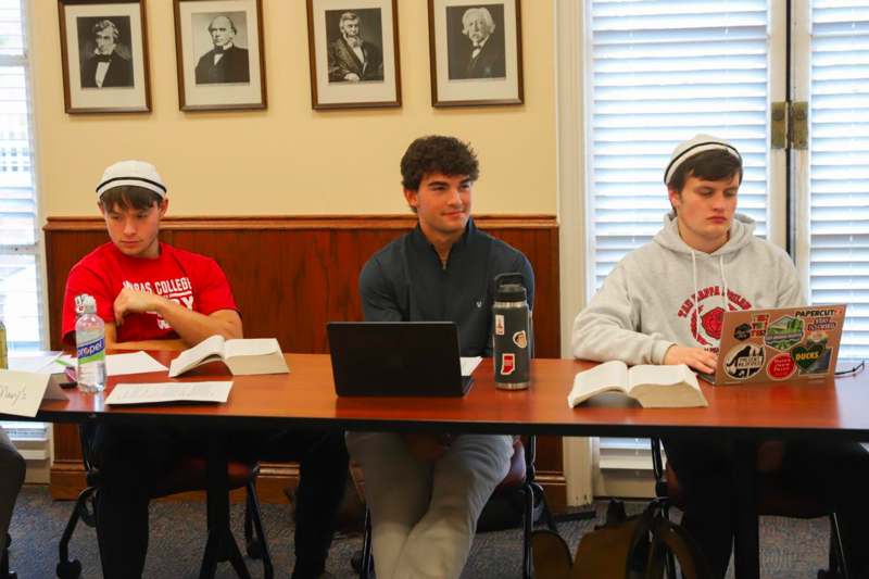 a group of people sitting at a table with books and laptops