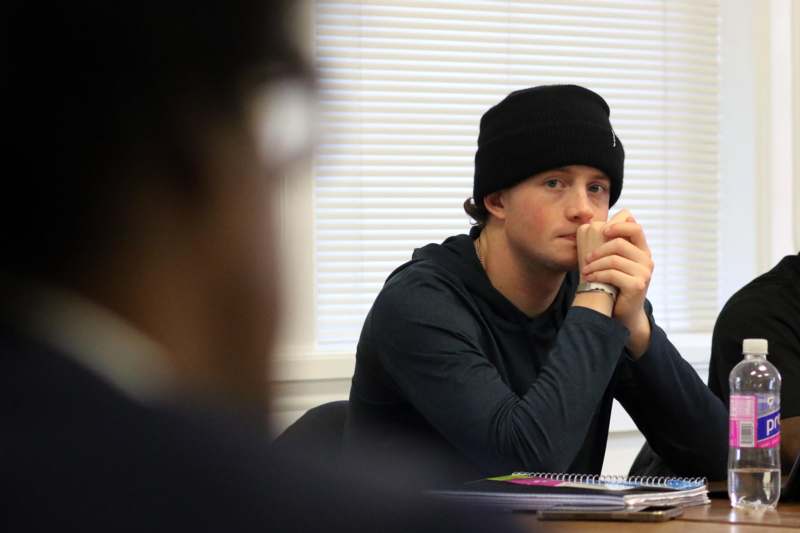 a man in a beanie sitting at a table with his hands folded