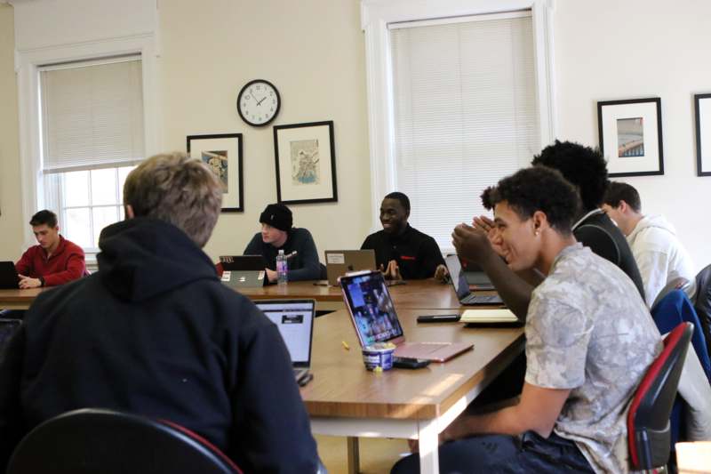 a group of people sitting around a table with laptops