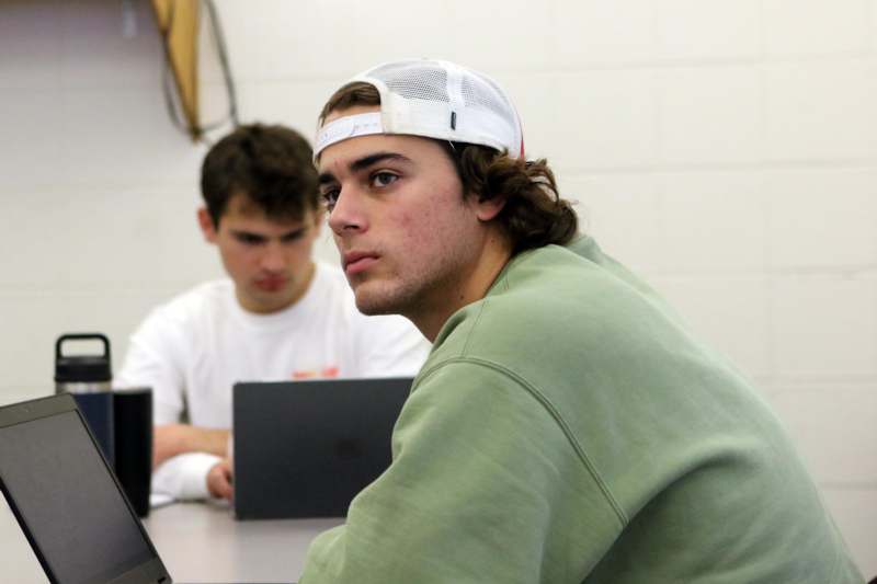 a man wearing a white hat and sitting at a table with another man in the background