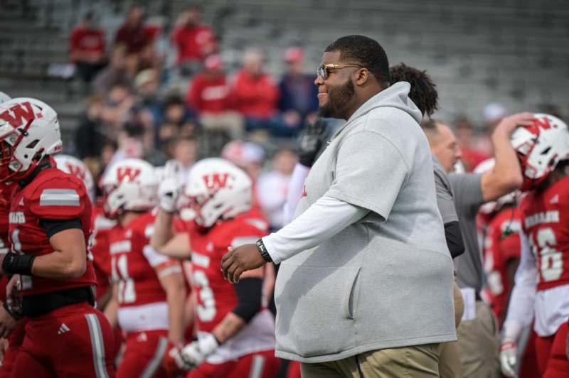 a man in a grey sweatshirt and tan pants standing on a field with other people in the background
