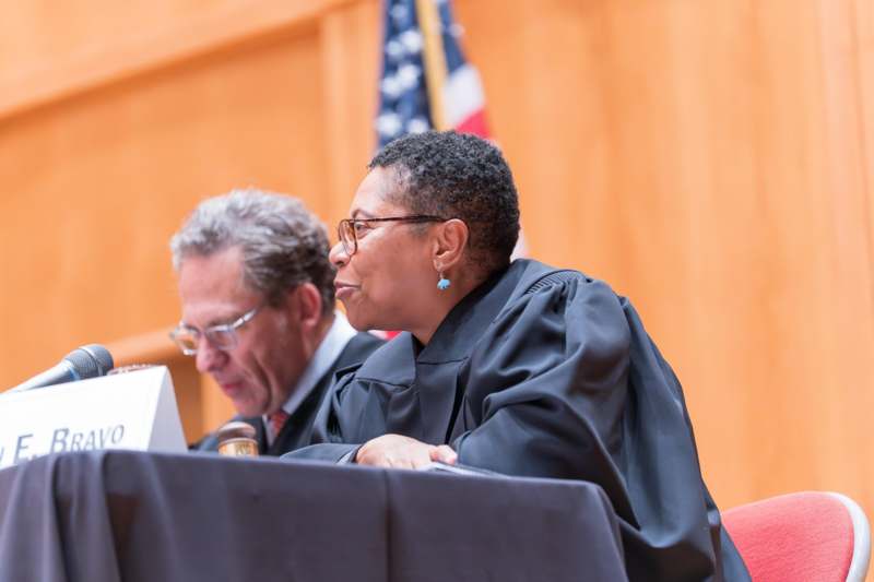 a woman in a black robe sitting at a table with a man in a courtroom