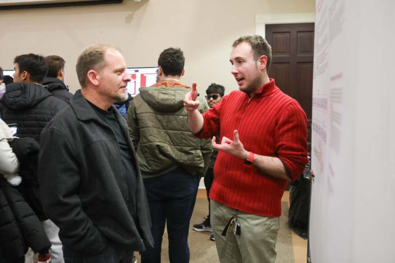 a man in a red sweater talking to another man in a room