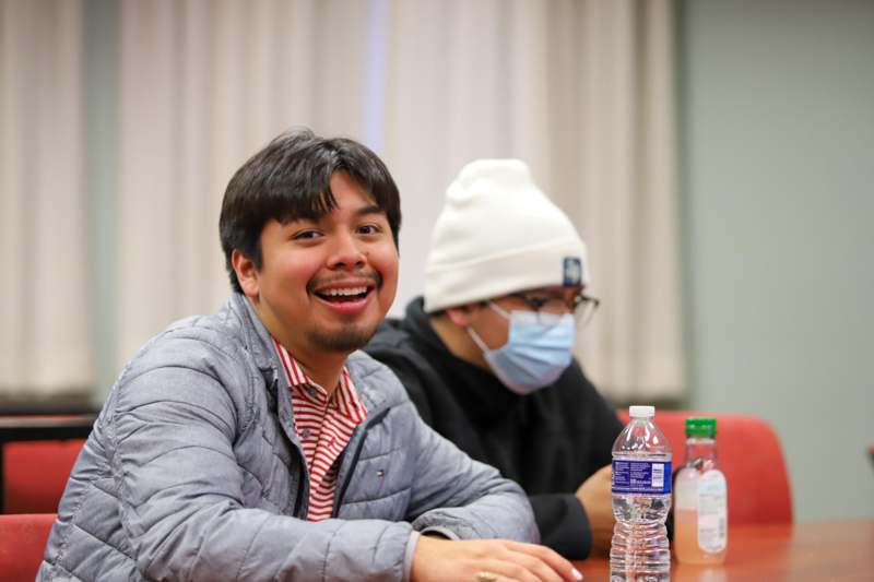 a man sitting at a table with a bottle of water and a man wearing a mask