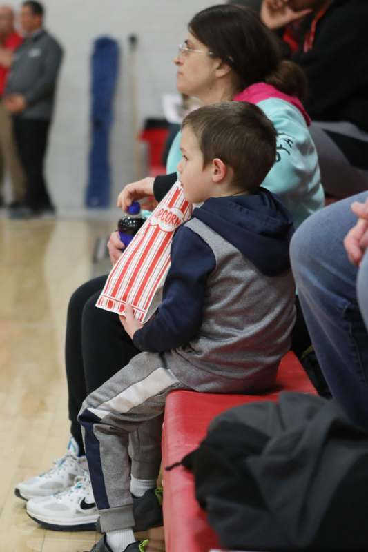 a boy sitting on a bench with a bag of popcorn
