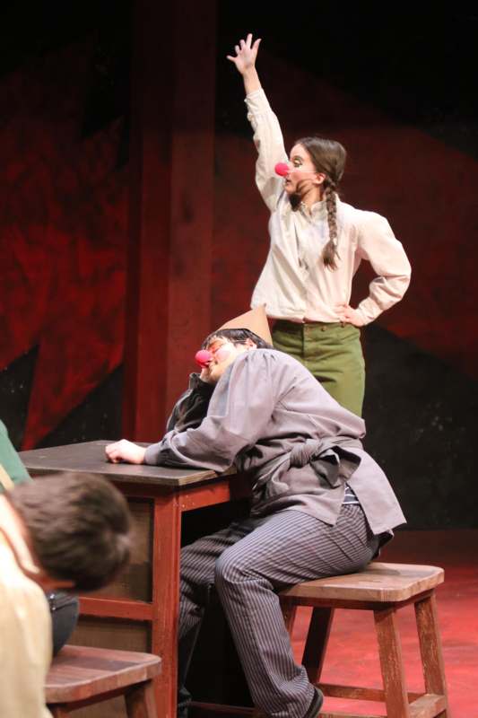 a woman with red clown nose and a man lying down on a desk