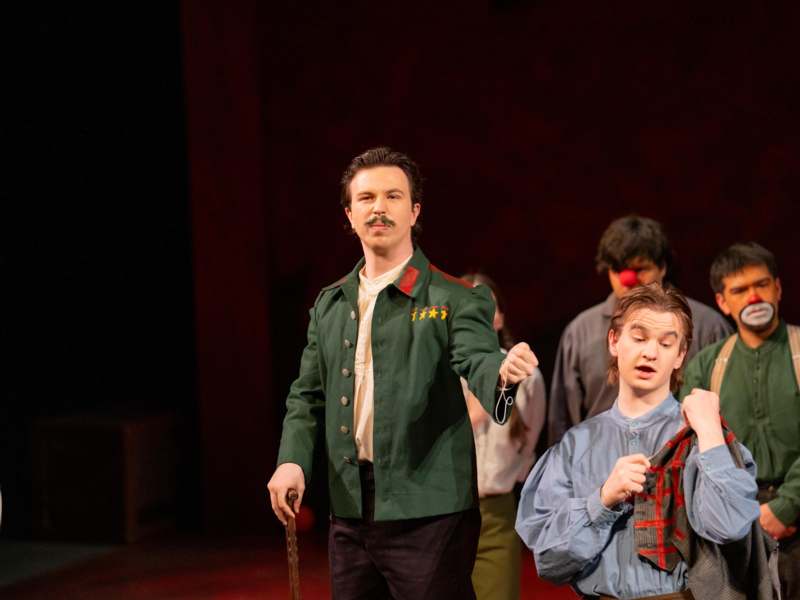 a man in a green jacket holding a cane and a man in a red clown garment