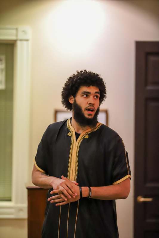 a man with curly hair and beard wearing a black and gold robe